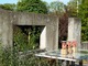 Ściany z surowego betonu z pustymi oknami, przez które roślinność "wdziera" się do ogrodu